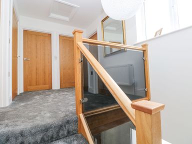 A hallway with wooden doors and carpeted floor with a wooden and glass stair railing at Golygfa Hafan in Little Haven
