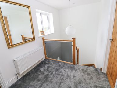 A stair landing area with gray carpet a wooden framed glass banister a radiator a window with a small frame and a large wall mirror at Golygfa Hafan in Little Haven