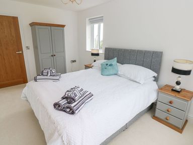 A bedroom with a double bed white bedspread gray headboard bedside tables with lamps gray wardrobe and towels on the bed at Golygfa Hafan in Little Haven