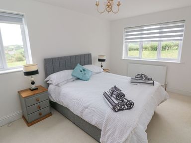 A bedroom with a double bed two nightstands with lamps two windows and rolled towels on the bed at Golygfa Hafan in Little Haven