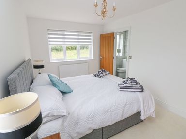 A bedroom with a made bed with white bedding and towels on it a window with striped blinds and an open door to a bathroom at Golygfa Hafan in Little Haven