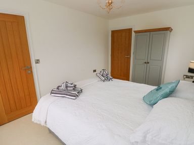 A bedroom with a white bedspread striped towels two wooden doors and a gray wardrobe at Golygfa Hafan in Little Haven