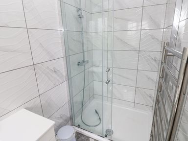 A bathroom with a glass enclosed shower area chrome towel warmer a white cabinet and a small round bin at Golygfa Hafan in Little Haven