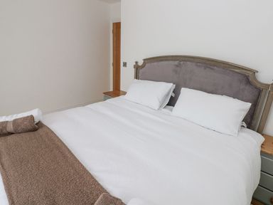 A bedroom with a large bed with white bedding two pillows brown towel and wooden bedside tables at Golygfa Hafan in Little Haven