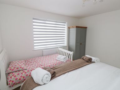 A bedroom with two beds a wardrobe and a window with striped blinds at Golygfa Hafan in Little Haven