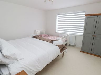 A bedroom with two beds a wardrobe and a window with blinds at Golygfa Hafan in Little Haven
