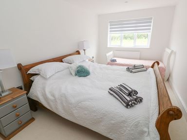 A bedroom with a wooden double bed with white bedding and a single bed near the window at Golygfa Hafan in Little Haven