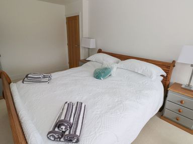 A bedroom with a wooden bed frame white bedding folded striped towels and bedside tables with lamps at Golygfa Hafan in Little Haven