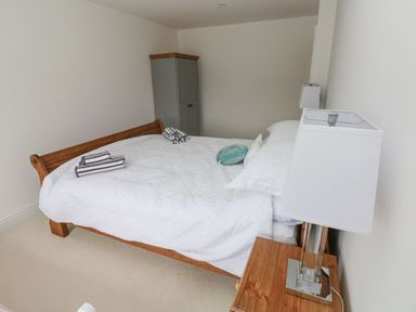 A bedroom with a wooden bed covered in white bedding two bedside tables with lamps and a grey wardrobe in the corner at Golygfa Hafan in Little Haven