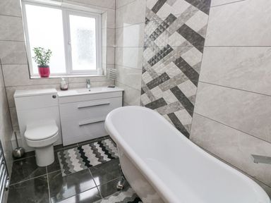 A bathroom with a white toilet sink vanity bathtub patterned wall tiles and a window with a plant at Golygfa Hafan in Little Haven