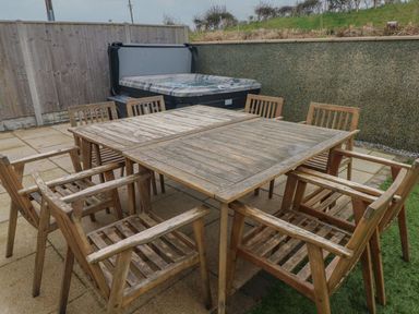 An outdoor patio area with a wooden table and eight wooden chairs next to a hot tub at Golygfa Hafan in Little Haven
