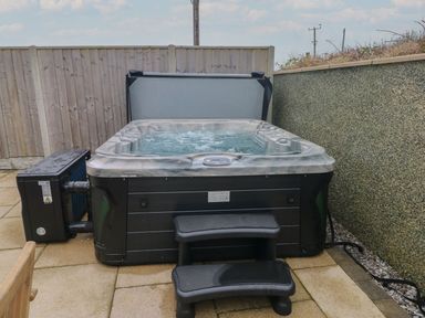An outdoor hot tub with steps on a paved patio between a wooden fence and a textured wall at Golygfa Hafan in Little Haven
