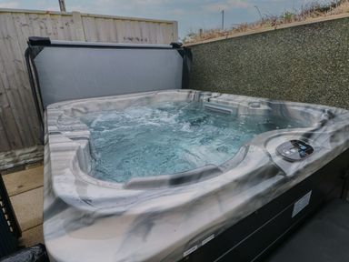 An outdoor hot tub with water jets next to a wooden fence and a stone wall at Golygfa Hafan in Little Haven