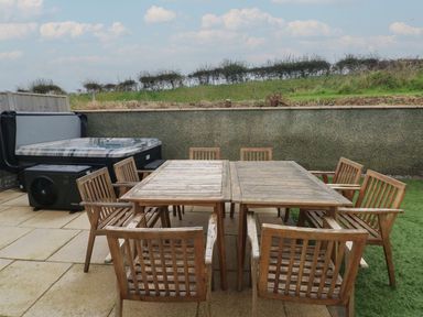 An outdoor patio with a wooden table and chairs and a hot tub in the corner at Golygfa Hafan in Little Haven