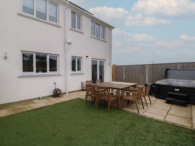 A backyard with wooden table and chairs a hot tub and artificial grass at Golygfa Hafan in Little Haven