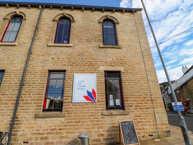 The exterior of a stone building with tall arched and rectangular windows a sign reading meet eat create enjoy and a chalkboard sign for a cafe at The Museum in Nenthead