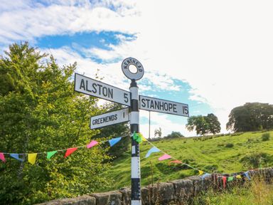 A road signpost showing directions to Alston Stanhope and Greenends with colorful bunting in a rural area at The Museum in Nenthead