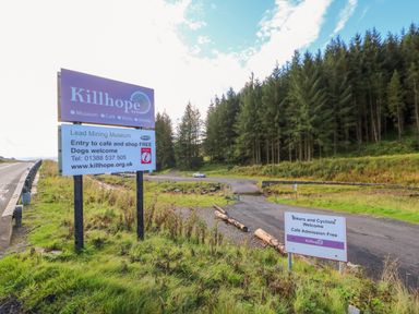 A road sign for Killhope Lead Mining Museum near a forest with a small parking area at The Museum in Nenthead