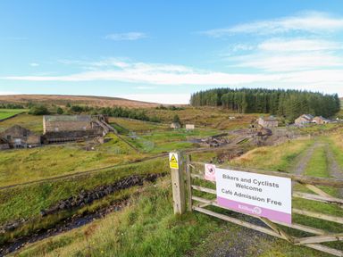 A rural area with old stone buildings fenced off and a gate with a sign welcoming bikers and cyclists at Killhope