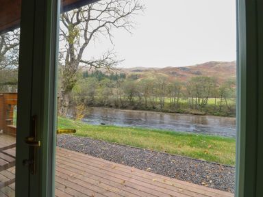 A view of a river trees and hills from a wooden deck outside a house at Bradan Lodge in Dalmally