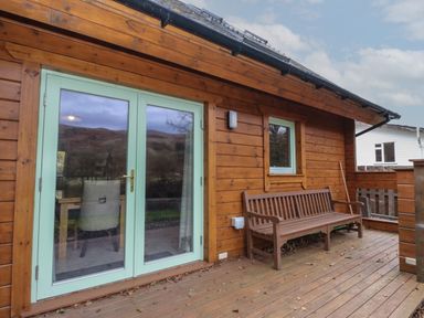 A wooden porch with a bench and glass double doors at Bradan Lodge in Dalmally