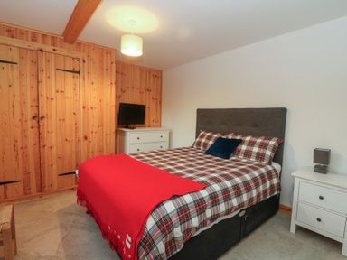 A bedroom with a bed a red blanket a white chest of drawers with a television and a white nightstand with a lamp at Bradan Lodge in Dalmally
