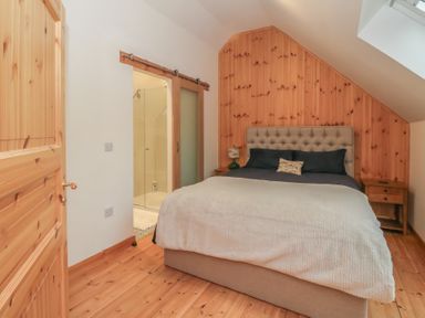 A bedroom with a bed two bedside tables a sliding door and wooden paneling at Bradan Lodge in Dalmally