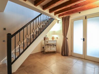 An entryway with a staircase railing a small mirrored cabinet with a lamp and frosted glass double doors at Bridge Barn in Sidestrand near Overstrand