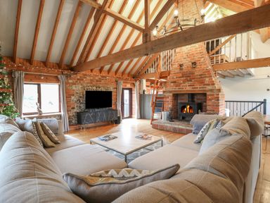 A living room with a large beige sectional sofa a central coffee table a brick fireplace exposed wooden beams and a television at Bridge Barn in Sidestrand near Overstrand