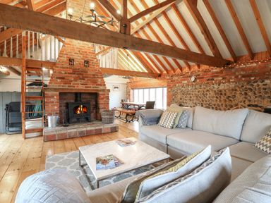 A living room with a brick fireplace wooden beams and a gray sofa at Bridge Barn in Sidestrand near Overstrand