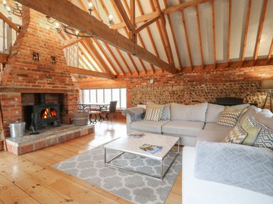 A living room with a brick fireplace a grey sectional sofa and a coffee table at Bridge Barn in Sidestrand near Overstrand
