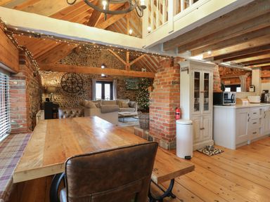 A rustic open plan kitchen and living area with wooden beams a dining table and a Christmas tree at Bridge Barn in Sidestrand near Overstrand
