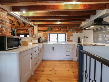 A kitchen with wooden beams exposed brick walls white cabinets and wooden floor at Bridge Barn in Sidestrand near Overstrand