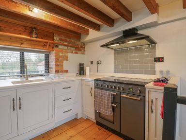 A kitchen with white cabinets a black stove a stainless steel sink and wooden ceiling beams at Bridge Barn in Sidestrand near Overstrand