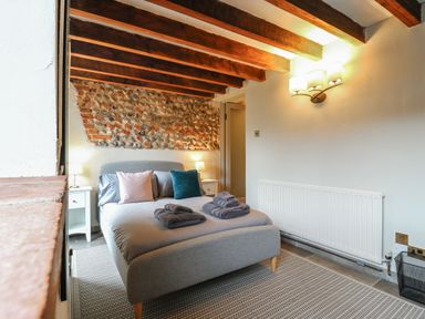 A bedroom with a double bed and towels on a rug with exposed beams and a stone wall at Bridge Barn in Sidestrand near Overstrand