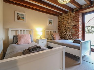 A bedroom with two white single beds with gray bedding and pink pillows a nightstand with a lamp and framed pictures on the wall at Bridge Barn in Sidestrand near Overstrand