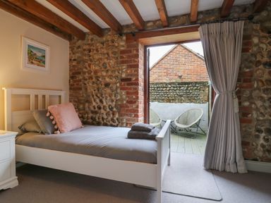 A bedroom with a white bed and gray bedding next to a door leading to an outdoor seating area at Bridge Barn in Sidestrand near Overstrand