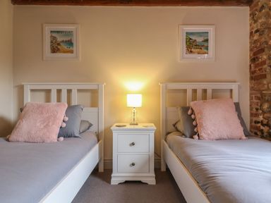 A bedroom with two single beds a nightstand with a lamp and framed pictures on the wall at Bridge Barn in Sidestrand near Overstrand