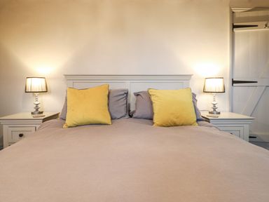 A bedroom with a bed with yellow pillows bedside tables with lamps and a sliding door at Bridge Barn in Sidestrand near Overstrand