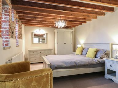 A bedroom with a bed yellow chairs white wardrobes and exposed wooden ceiling beams at Bridge Barn in Sidestrand near Overstrand