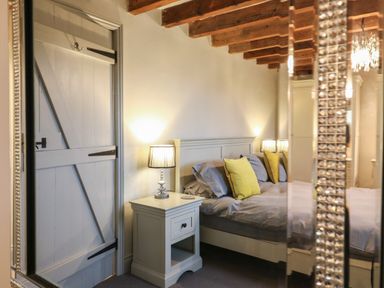 A bedroom with a bed with pillows bedside table with a lamp and wooden door at Bridge Barn in Sidestrand near Overstrand