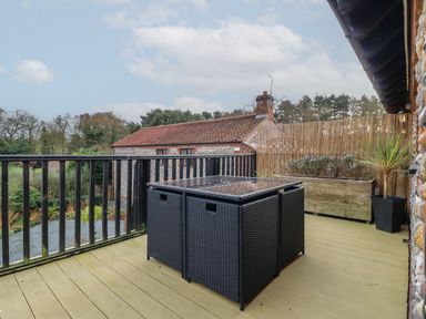 An outdoor balcony with a black table and chairs and a planter with plants at Bridge Barn in Sidestrand near Overstrand