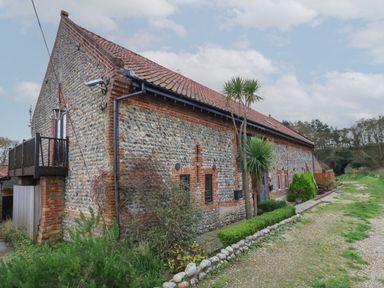 A stone and brick barn with small windows and a tiled roof with plants along the side at Bridge Barn in Sidestrand near Overstrand