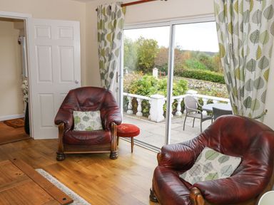 A sitting area with two leather armchairs and patterned curtains by sliding glass doors at Lakeview Lodge in Knockmore County Mayo
