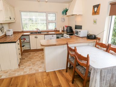 A kitchen with wooden countertops and floor a dining table with a white tablecloth and wooden chairs a window and various appliances at Lakeview Lodge in Knockmore County Mayo
