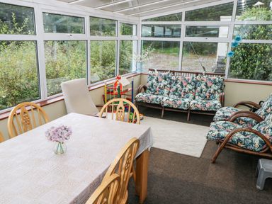 A sunroom with a dining table and chairs a floral sofa set and large windows at Lakeview Lodge in Knockmore County Mayo