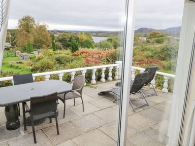 A patio with a table and chairs and two lounge chairs overlooking a garden and lake at Lakeview Lodge in Knockmore County Mayo