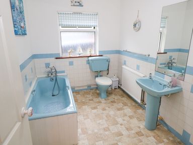 A bathroom with a blue bathtub toilet and sink with tiled walls and a window at Lakeview Lodge in Knockmore County Mayo