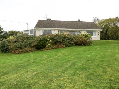 A bungalow with a tiled roof and shrubbery in front on a grassy lawn at Lakeview Lodge in Knockmore County Mayo