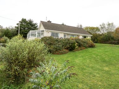 A bungalow house with a glass porch and garden shrubs on a grassy lawn at Lakeview Lodge in Knockmore County Mayo
